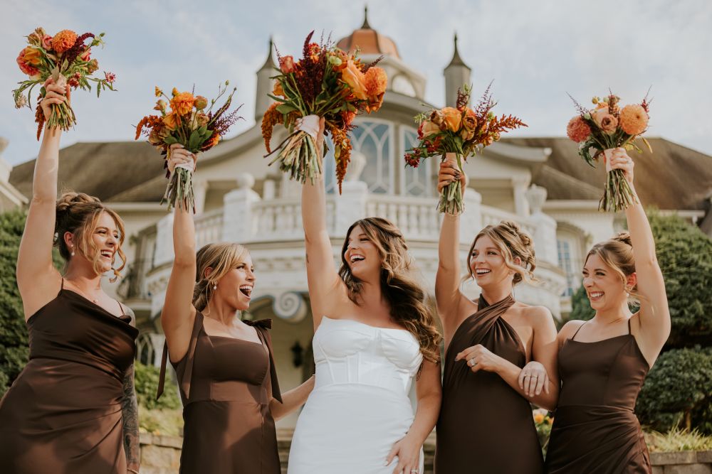 Bridal party holding flowers up in front of the estate